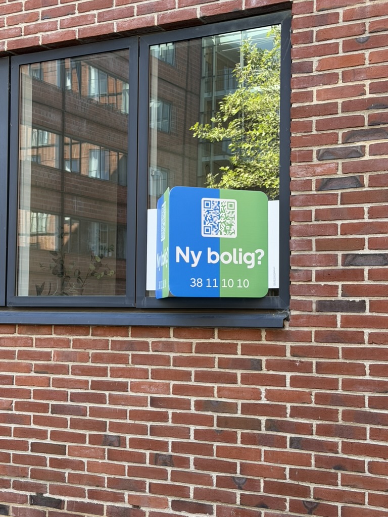 Vinkelskilt med QR-kode og telefonnummer på facadevindue